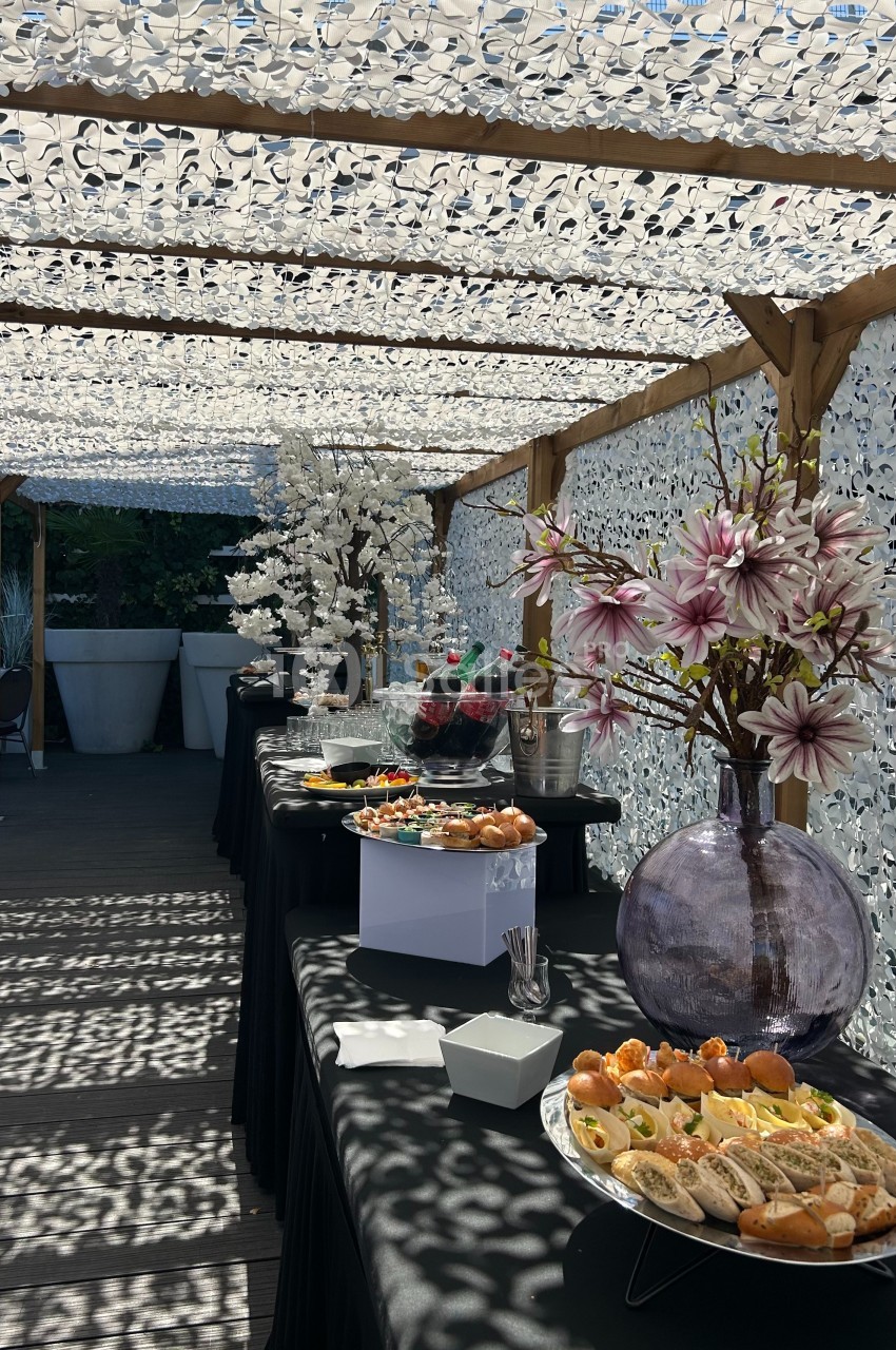 Buffet en extérieur sous une pergola ombragée, avec des plats variés et des décorations florales.