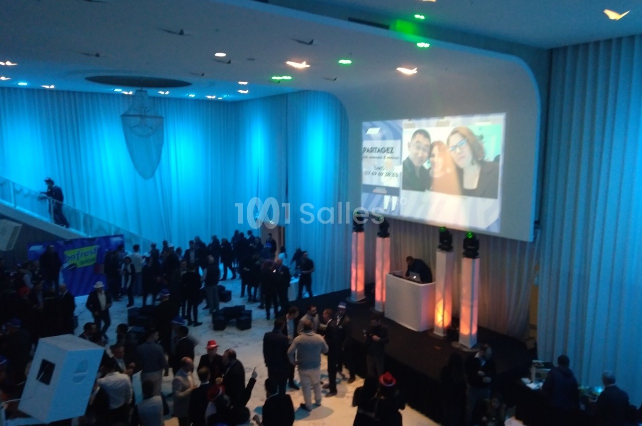 Salle de réception avec des invités rassemblés, éclairage bleu et projection d'images sur un mur.