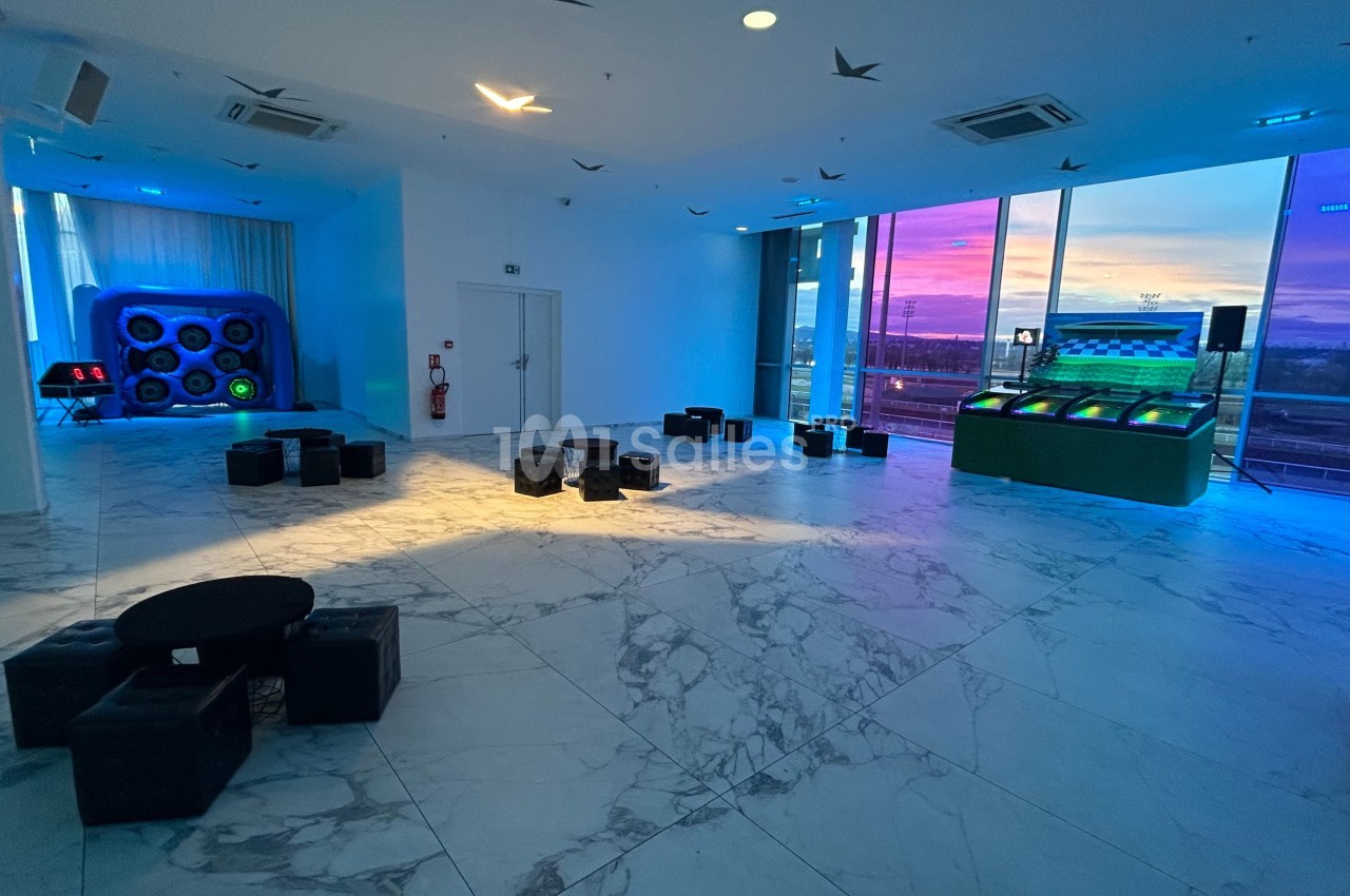 Salle moderne avec sol en marbre, jeux interactifs lumineux et vue sur un coucher de soleil à travers de grandes baies…
