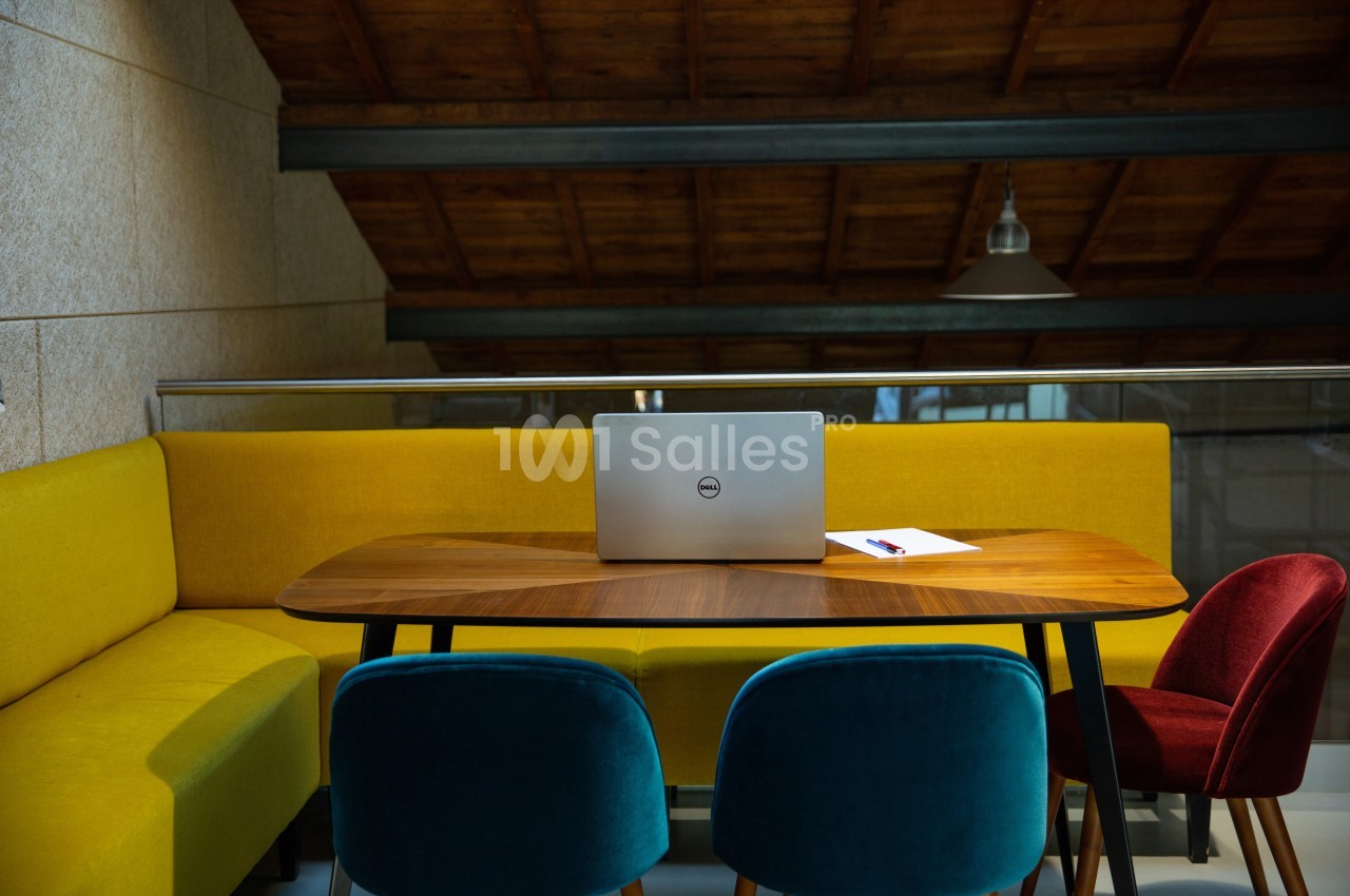 Ordinateur portable posé sur une table en bois entourée de chaises colorées dans une pièce au plafond en bois.