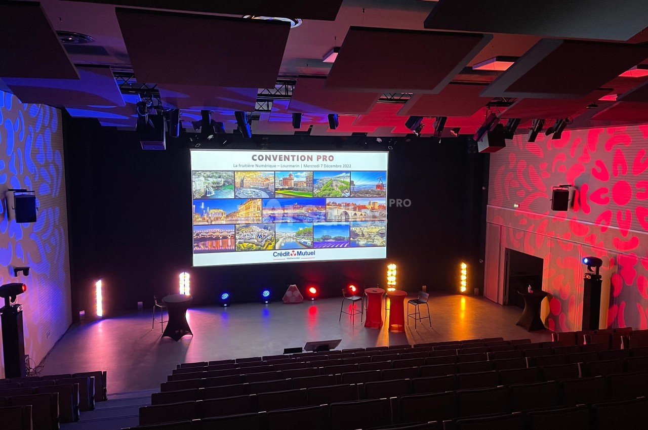 Salle de conférence vide avec un écran projetant des images et des lumières colorées illuminant la scène.