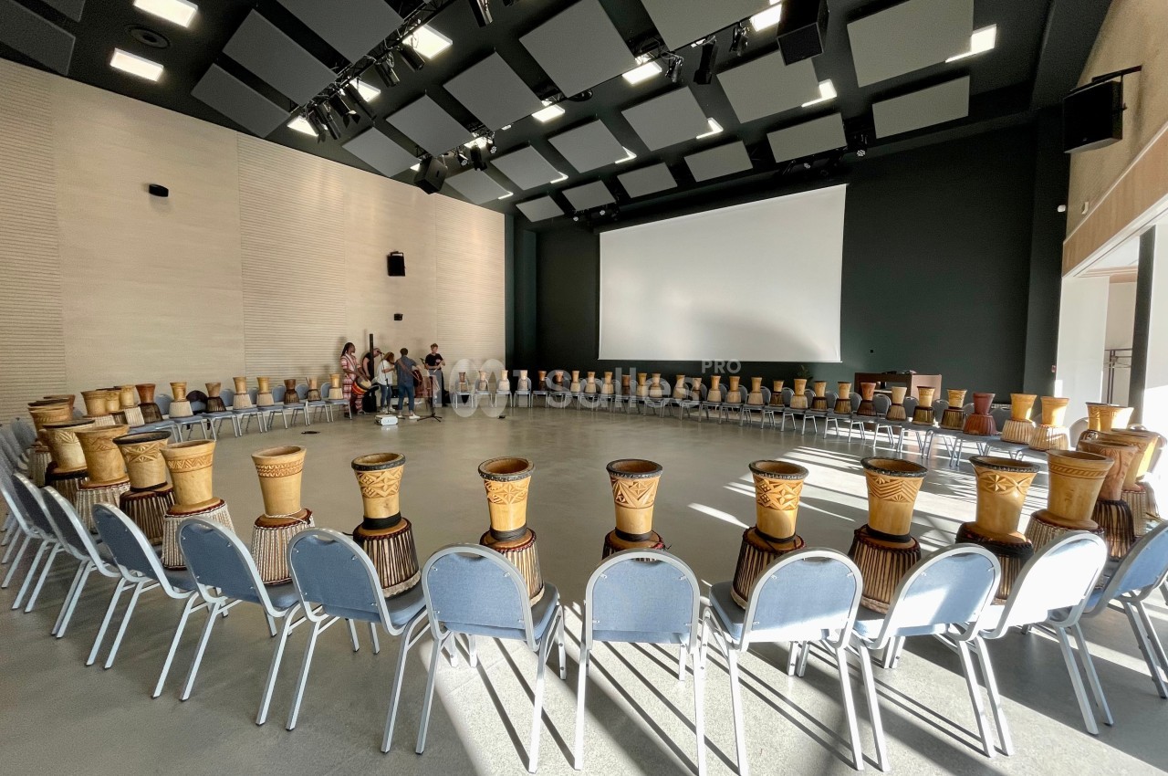 Salle lumineuse avec des chaises disposées en cercle, chacune équipée d'un djembé en bois sculpté.