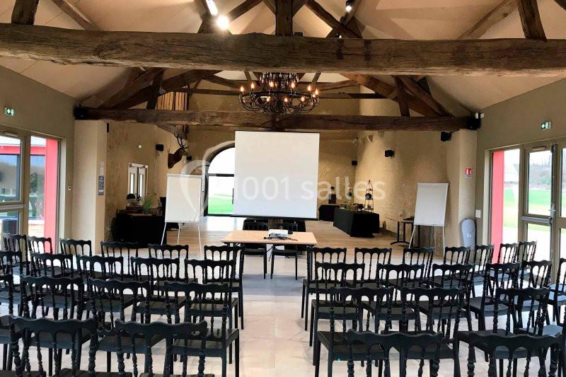 Salle de réunion avec poutres apparentes, chaises alignées, écran de projection et tableaux blancs.