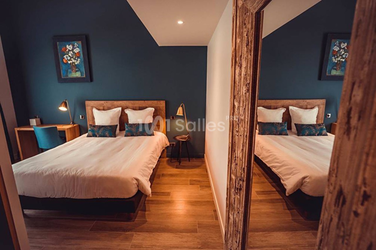 Chambre avec lit double, mur bleu, bureau en bois, lampe de chevet et miroir reflétant l'ensemble.