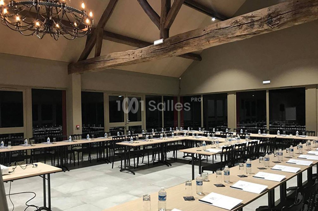 Salle de réunion spacieuse avec de longues tables disposées en U, équipée de bouteilles d'eau et de documents.