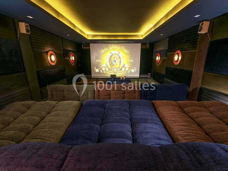 Salle de cinéma privée avec sièges en gradins rembourrés et écran affichant le logo d'un studio de production.