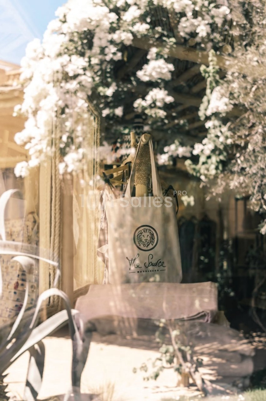 Sac en toile beige posé sur une chaise, entouré de plantes et de fleurs blanches dans un décor lumineux.