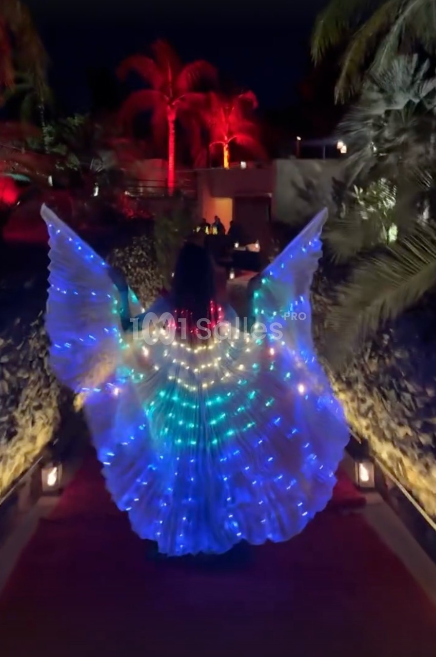 Personne portant une robe lumineuse avec des motifs colorés, avançant sur un chemin éclairé entouré de végétation tropicale.