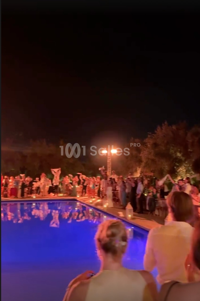 Des personnes rassemblées autour d'une piscine éclairée la nuit, certaines tenant des objets lumineux.
