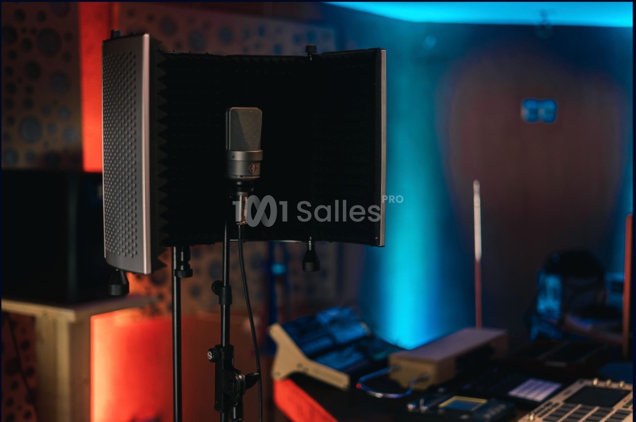 Microphone sur pied avec écran acoustique dans un studio d'enregistrement éclairé par des lumières colorées.