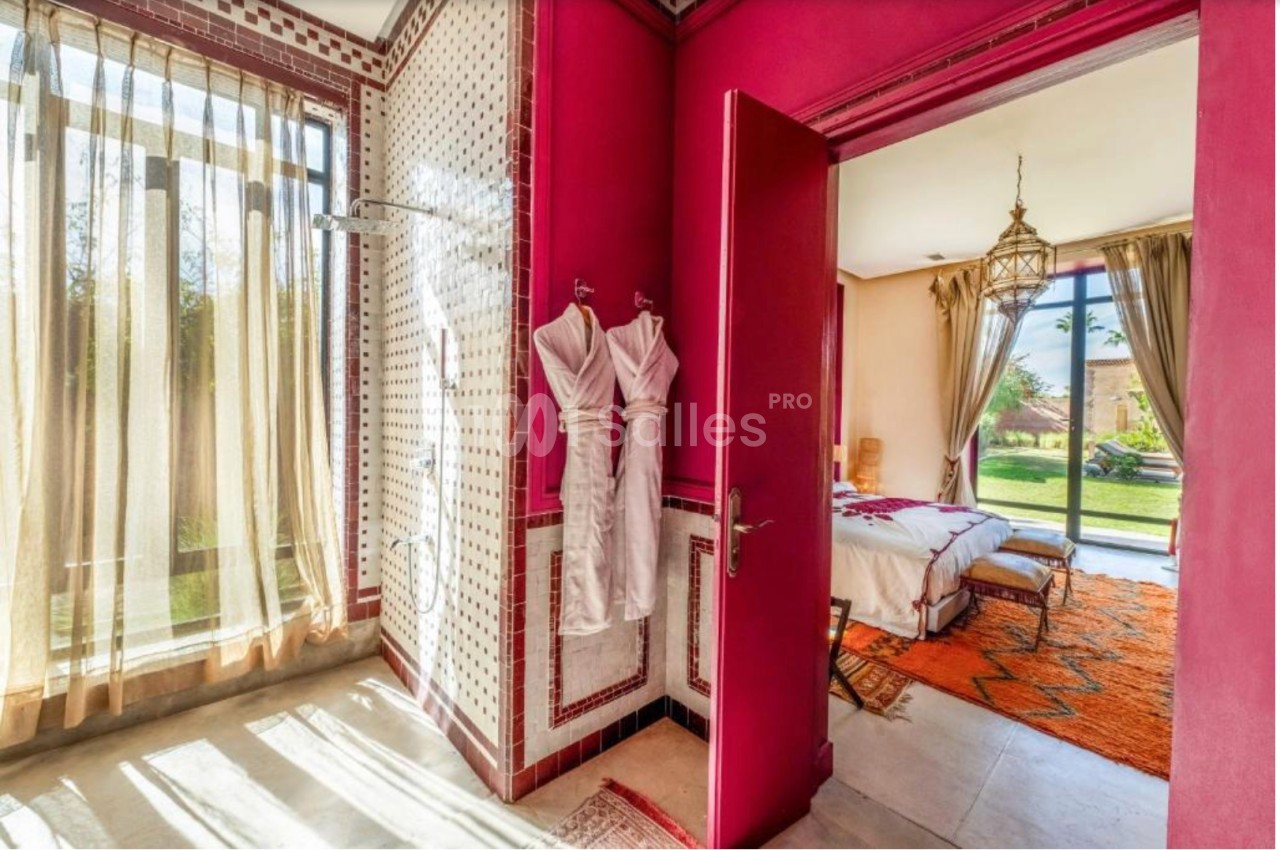 Salle de bain avec douche et peignoirs, ouverte sur une chambre lumineuse avec vue sur un jardin.