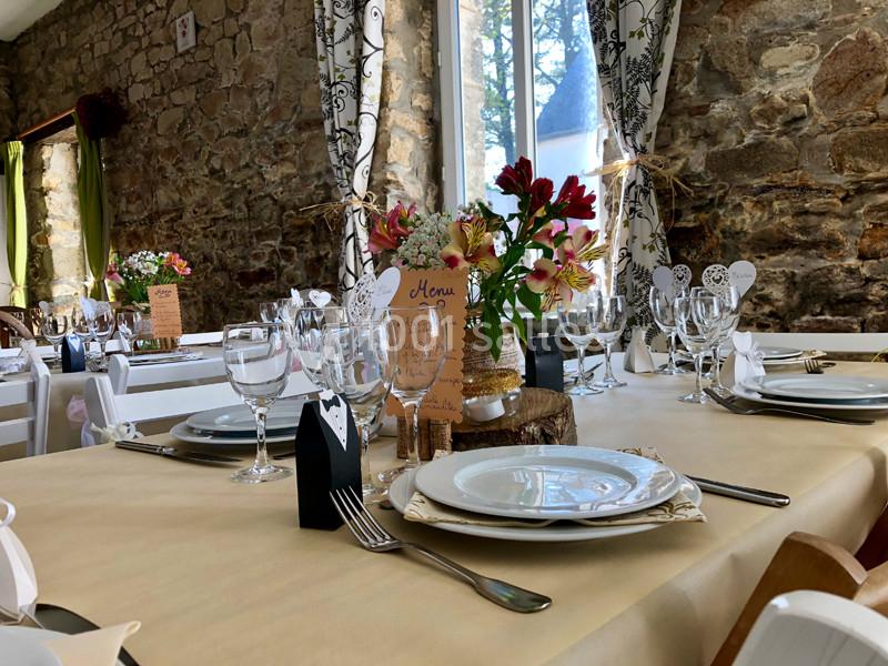 Table décorée pour un repas festif avec vaisselle élégante, fleurs colorées et menus en papier sur une nappe beige.