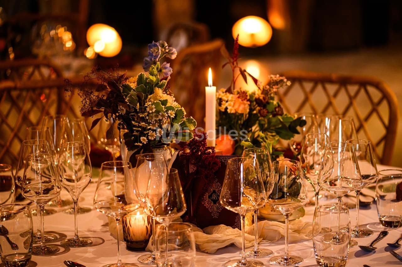 Table élégamment dressée avec bougies allumées, verres à vin et compositions florales dans une ambiance chaleureuse.