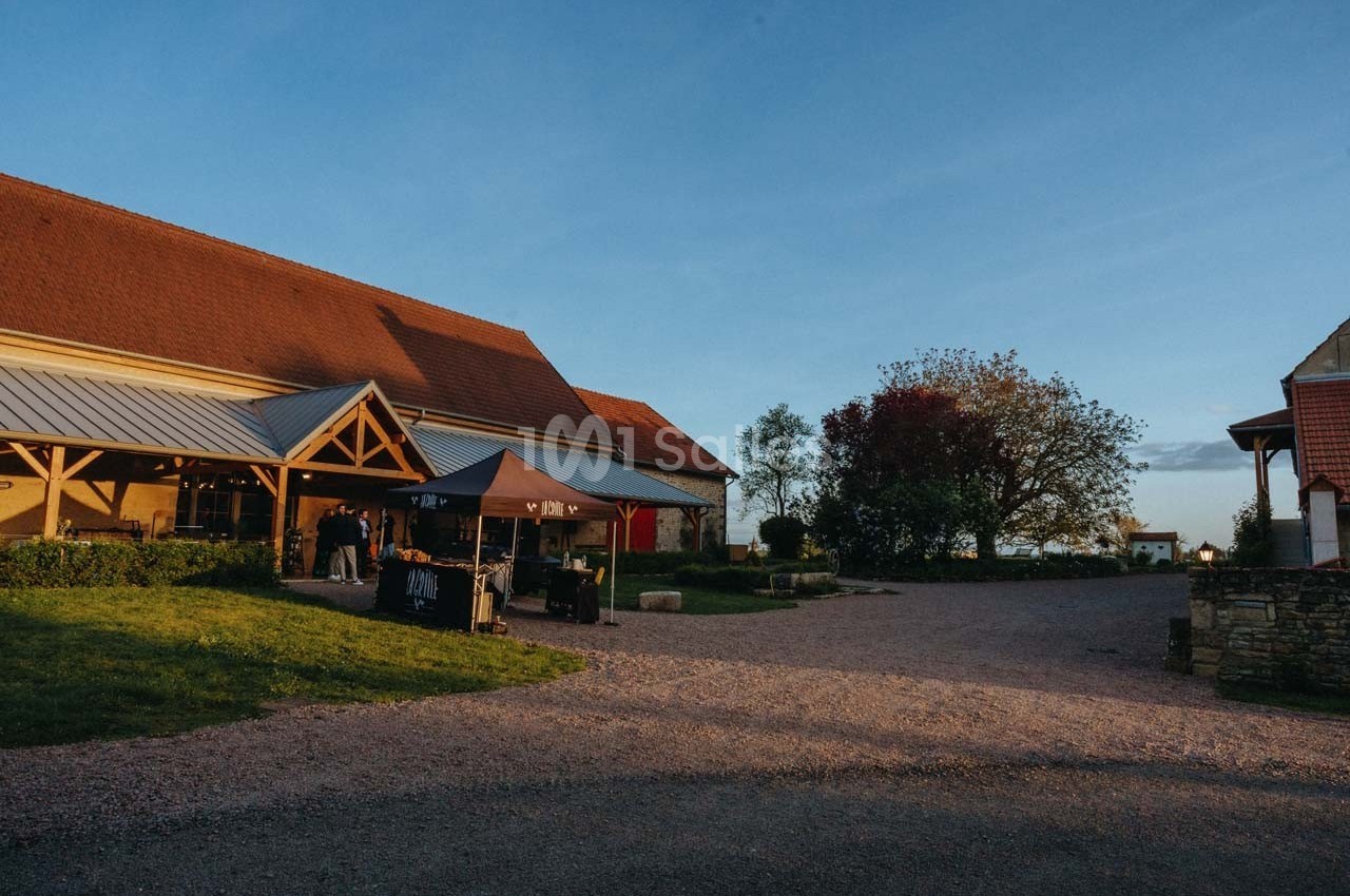 Bâtiment rural en pierre avec toit en tuiles, espace extérieur aménagé et ciel dégagé en fin de journée.