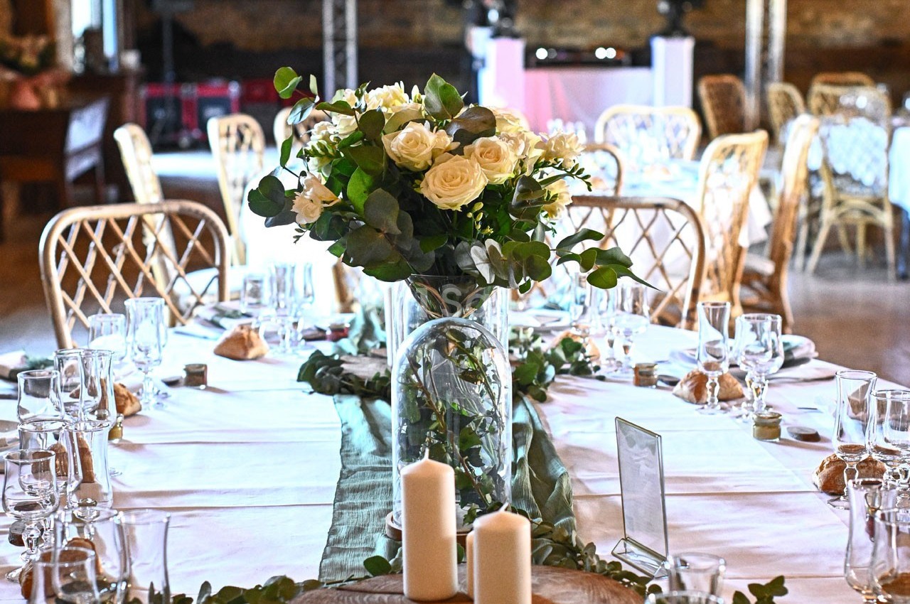 Table décorée pour un événement avec fleurs blanches, bougies et vaisselle élégante dans une salle rustique.