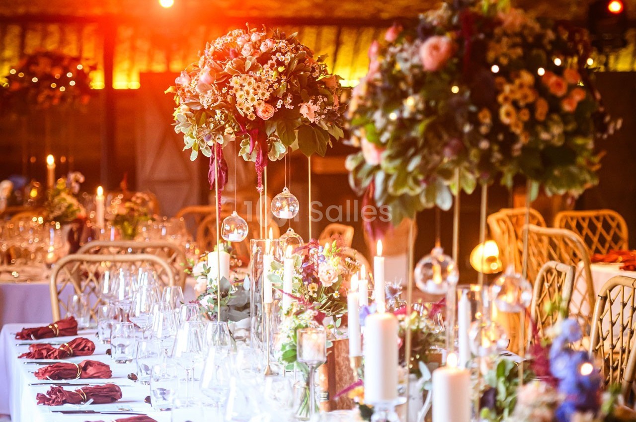 Tables décorées pour un événement avec chandeliers, compositions florales suspendues et lumière tamisée.