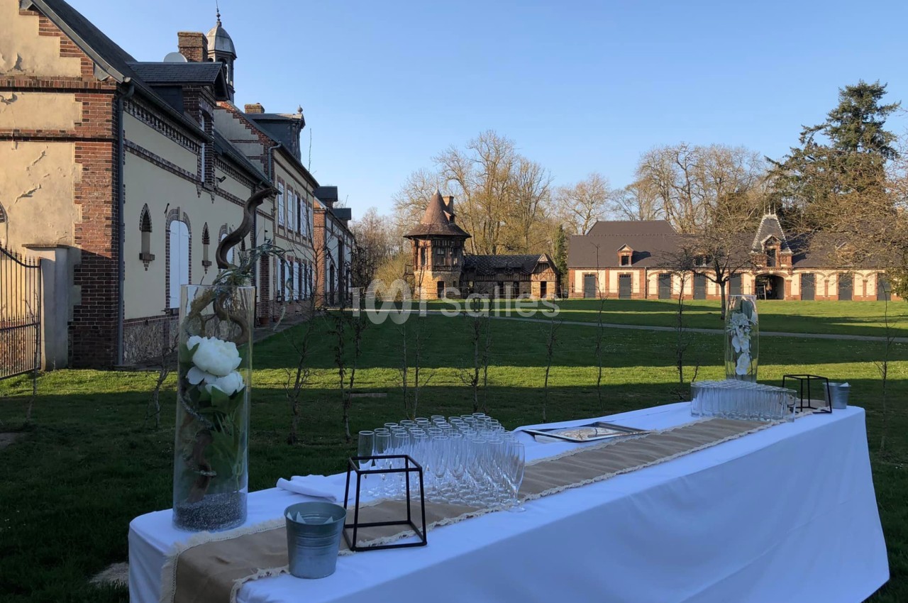 Table dressée avec des verres et des décorations florales devant un bâtiment en briques dans un cadre verdoyant.
