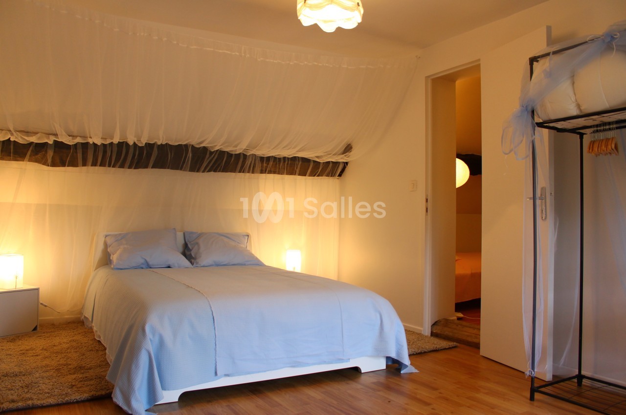 Chambre lumineuse avec lit double, draps bleus, moustiquaire suspendue et éclairage doux.