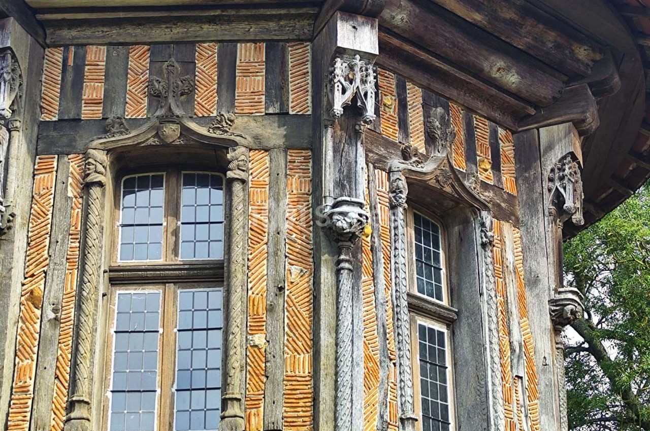 Façade d'une maison à colombages avec des motifs en briques et des sculptures en bois autour des fenêtres.