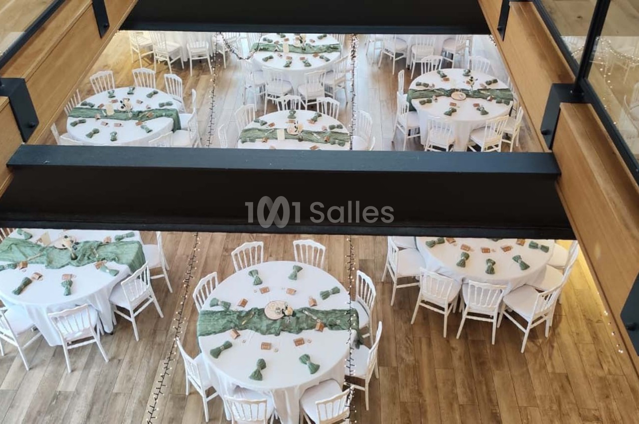 Vue plongeante sur une salle de réception avec des tables rondes décorées de nappes vertes et de chaises blanches.
