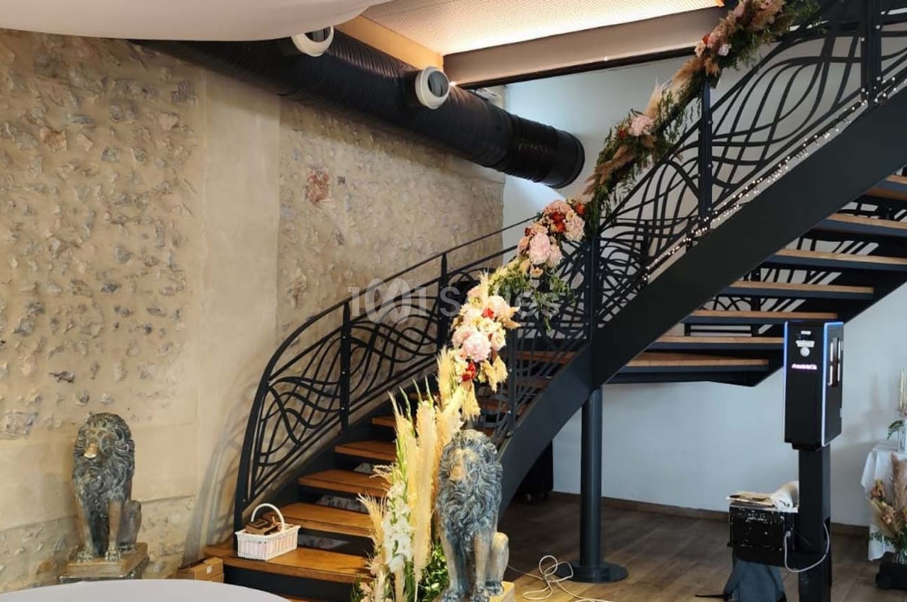 Escalier en métal décoré de fleurs, situé dans un intérieur avec murs en pierre et table ornée à droite.
