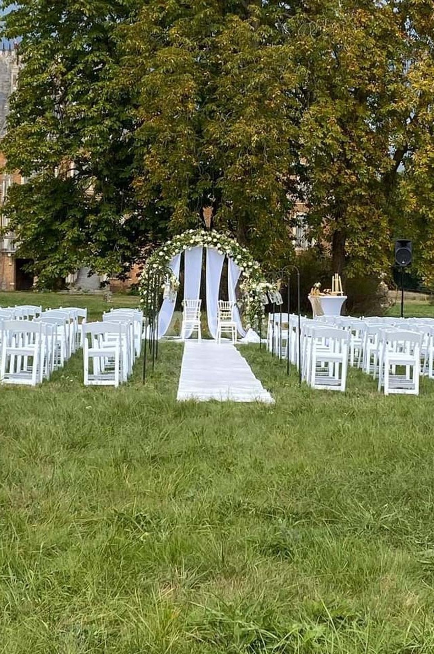 Allée centrale bordée de chaises blanches menant à une arche fleurie pour une cérémonie en plein air.