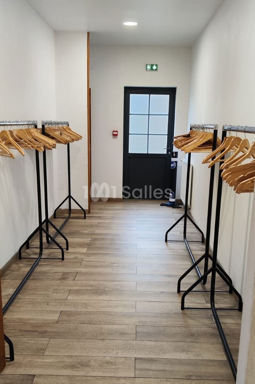 Portant en métal noir avec cintres en bois alignés de chaque côté d'un couloir au sol en parquet clair.