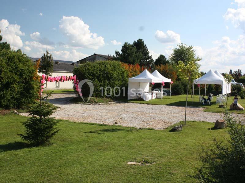 Jardin avec pelouse, tentes blanches, décorations roses et allée gravillonnée sous un ciel partiellement nuageux.