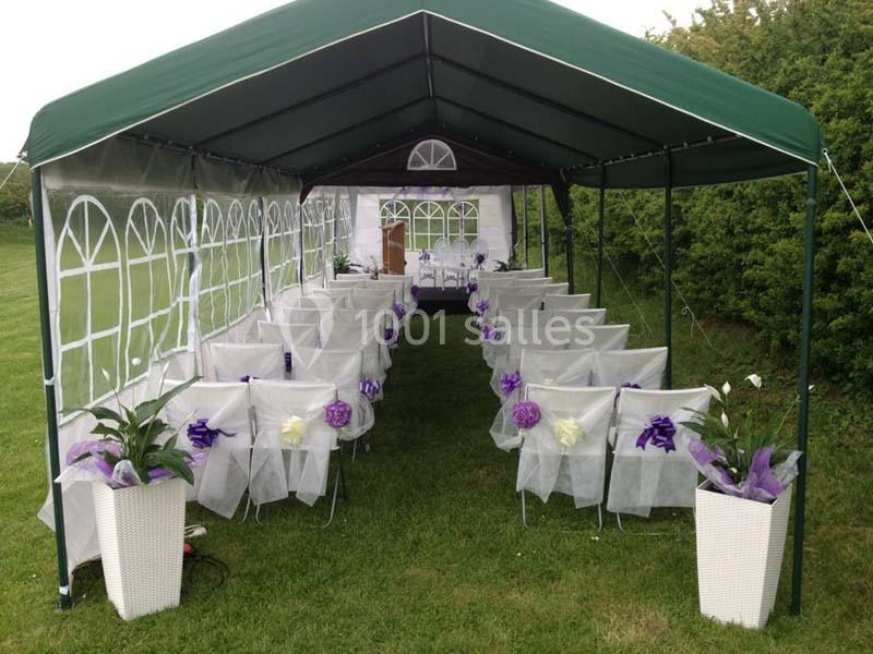 Tente de réception avec chaises décorées de rubans violets et blancs, disposées en rangées sur une pelouse.
