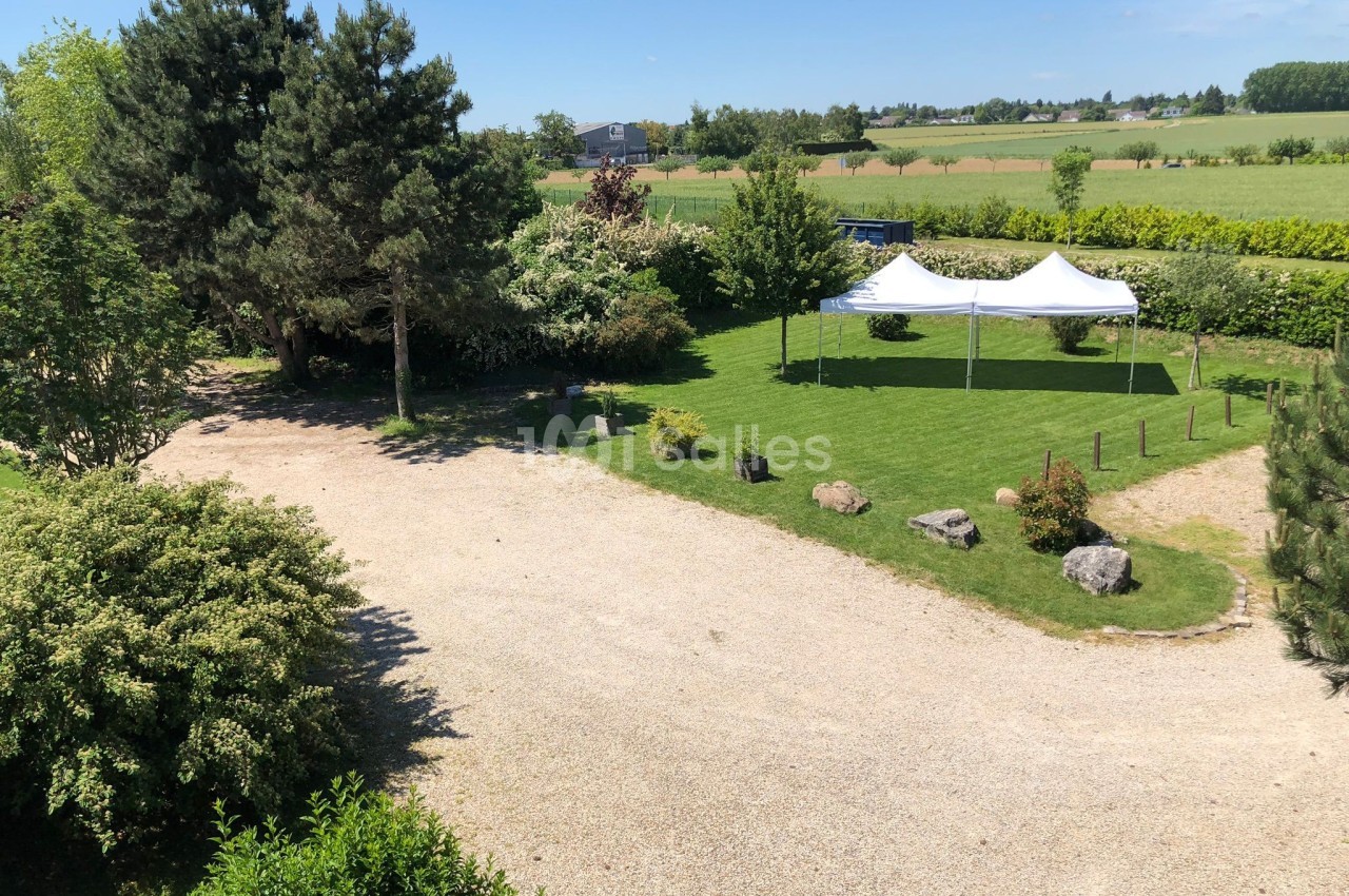 Vue d'un jardin avec pelouse, arbres, allée gravillonnée et deux tentes blanches installées sur le gazon.