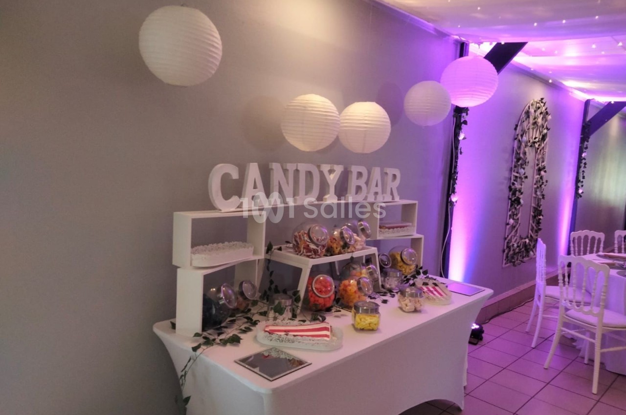 Table de candy bar décorée avec des bonbons variés, lanternes suspendues et éclairage violet en arrière-plan.