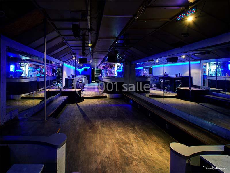 Salle de club vide avec éclairage bleu, miroirs sur les murs et bar au fond.