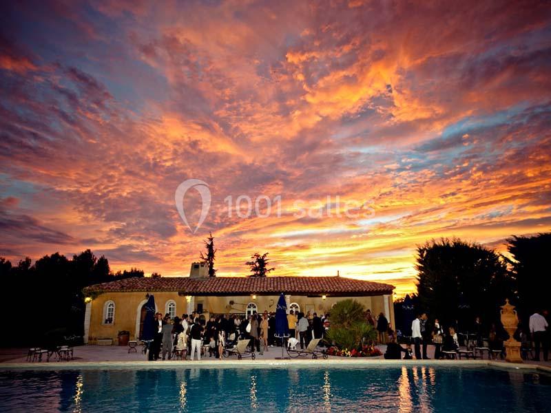 Coucher de soleil vibrant au-dessus d'une villa avec piscine, entourée d'invités lors d'un événement en plein air.
