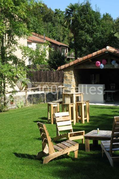 Espace extérieur avec pelouse, chaises en bois, table basse et abri décoré de ballons sous un ciel dégagé.