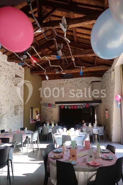 Salle décorée pour une fête avec tables dressées, ballons colorés et guirlandes suspendues sous un plafond en bois.