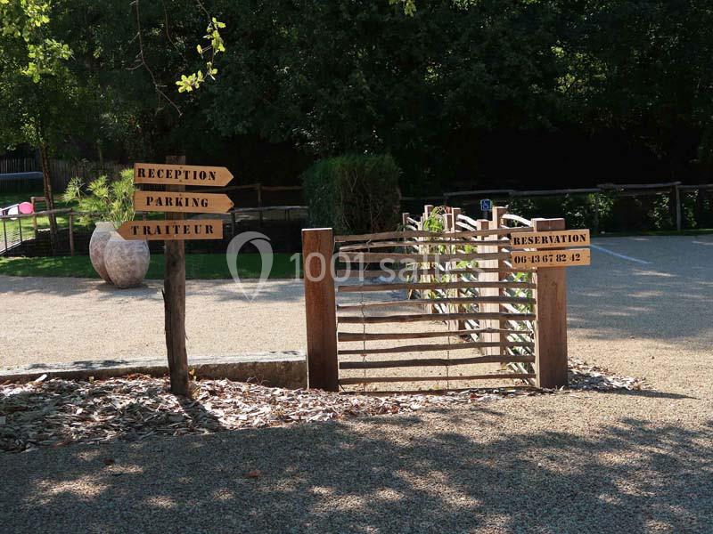 Panneau en bois indiquant réception, parking et traiteur, près d'une barrière en bois dans un espace extérieur arboré.