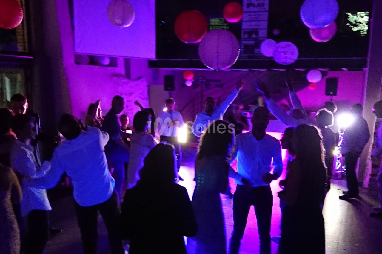 Groupe de personnes dansant dans une salle faiblement éclairée, décorée de lanternes suspendues.