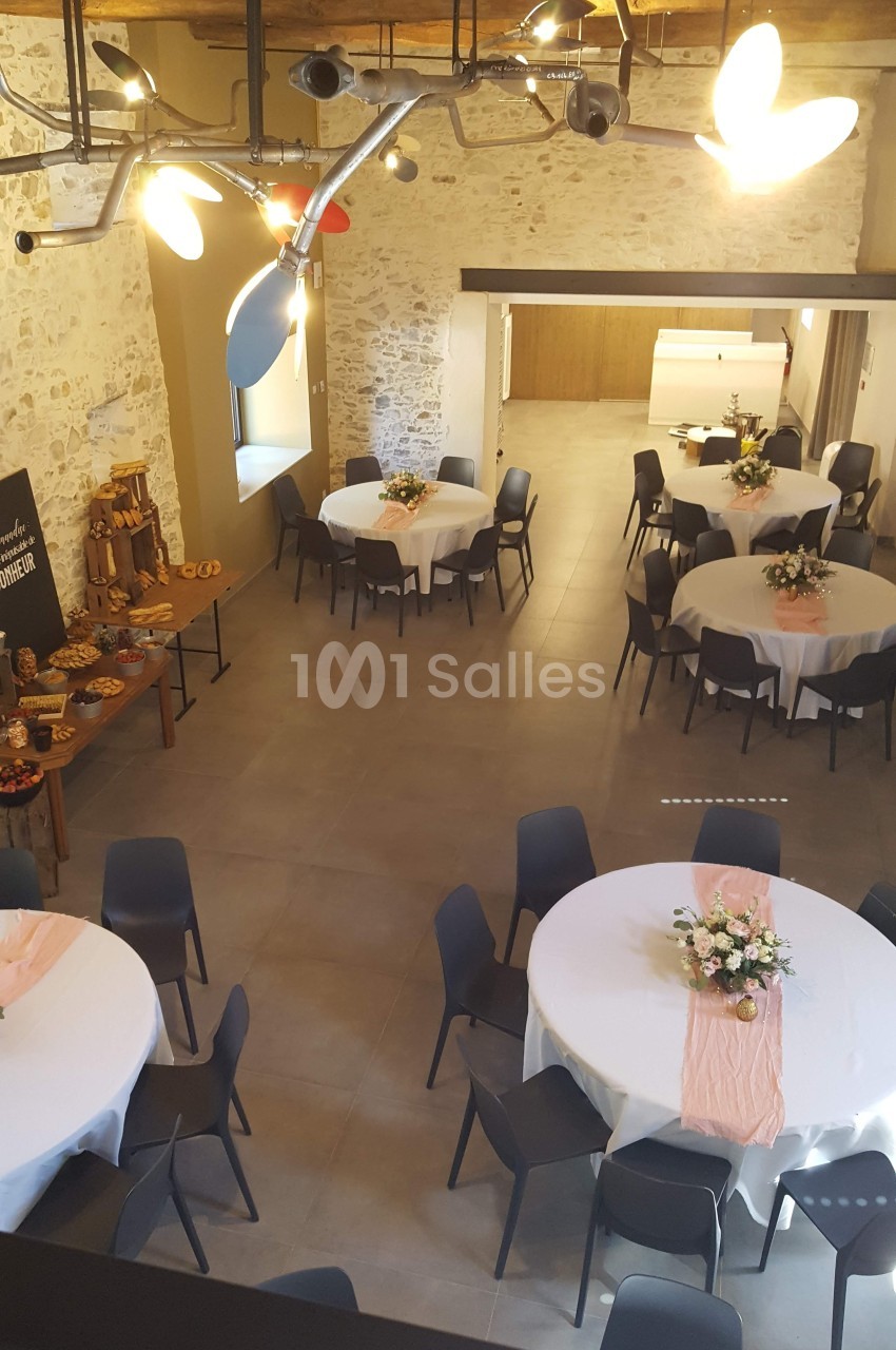 Salle de réception avec tables rondes décorées, chaises noires et buffet disposé sur une table en bois.