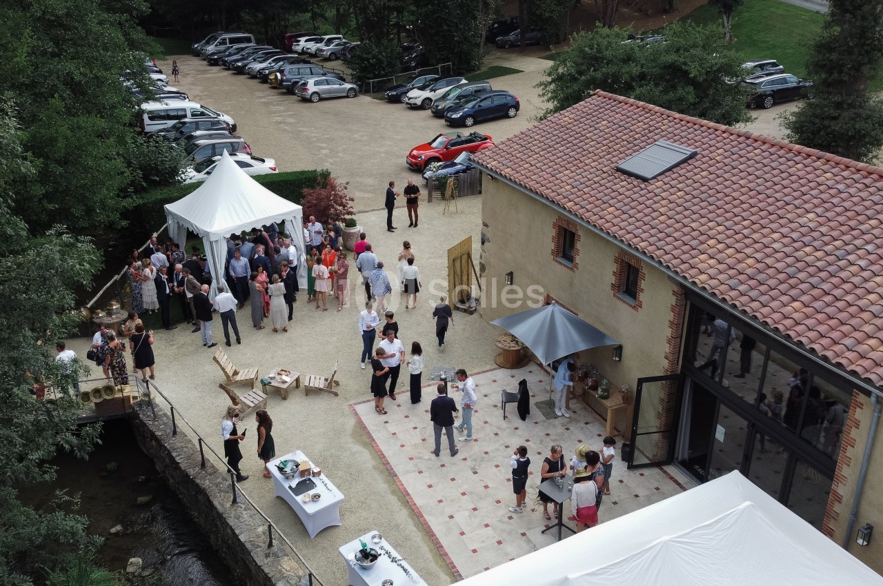 Vue aérienne d'un événement en plein air avec des invités rassemblés près d'une bâtisse et de tentes blanches.
