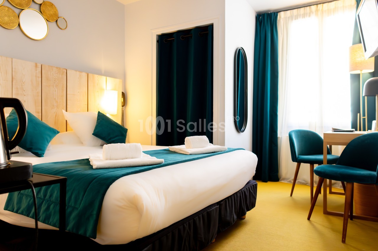 Chambre lumineuse avec lit double, draps blancs, coussins verts, bureau, chaises et rideaux assortis.