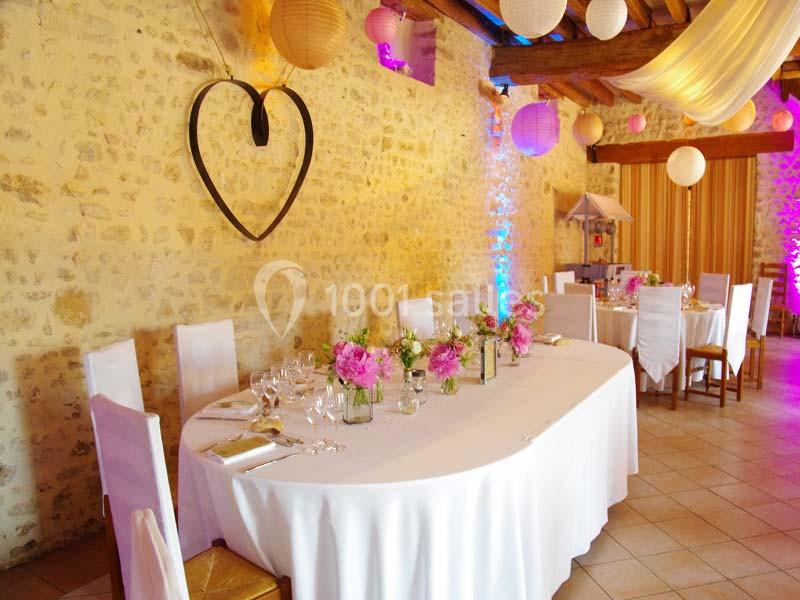 Salle de réception décorée avec des tables blanches, des fleurs roses et des lanternes suspendues.