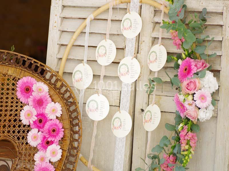 Cercle en bois décoré de fleurs roses et blanches, avec des cartes suspendues affichant des motifs floraux.
