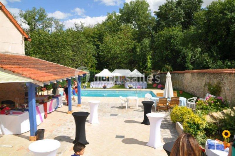 Espace extérieur avec piscine, tables dressées, tentes blanches et verdure environnante sous un ciel dégagé.