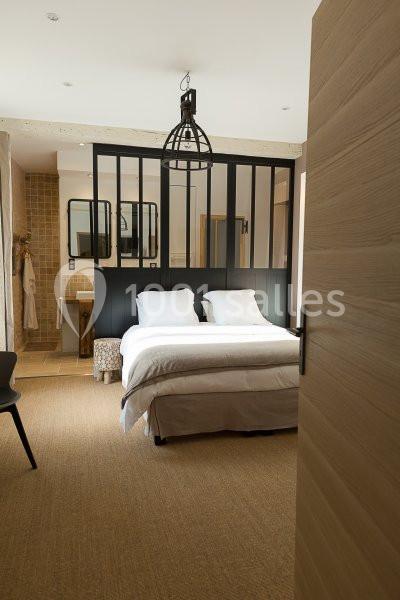 Chambre lumineuse avec lit double, verrière noire, salle de bain attenante et décoration moderne en bois et tons neutres.