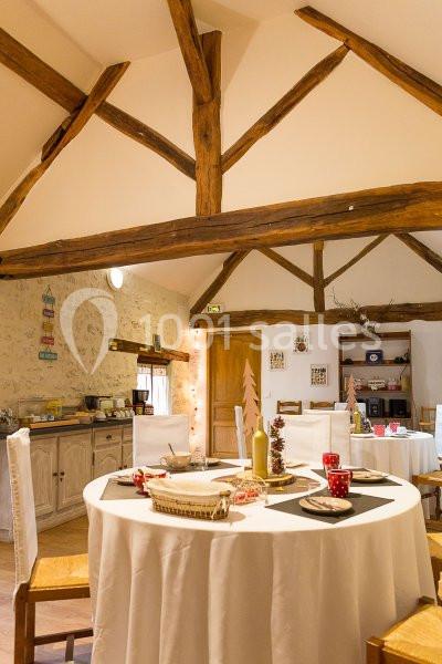 Salle à manger lumineuse avec des tables rondes dressées, poutres apparentes et un buffet en arrière-plan.