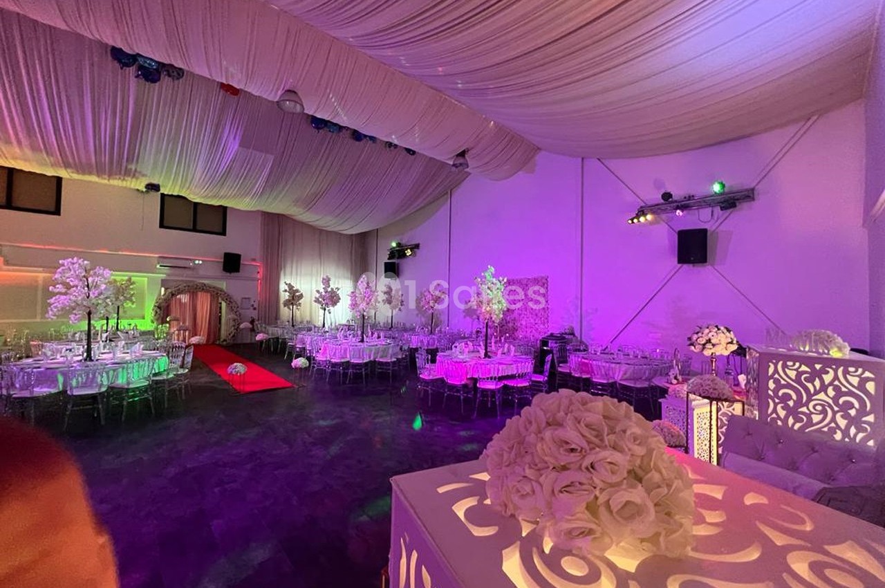 Salle de réception décorée avec des tables rondes, des chaises transparentes, des fleurs et un éclairage coloré.