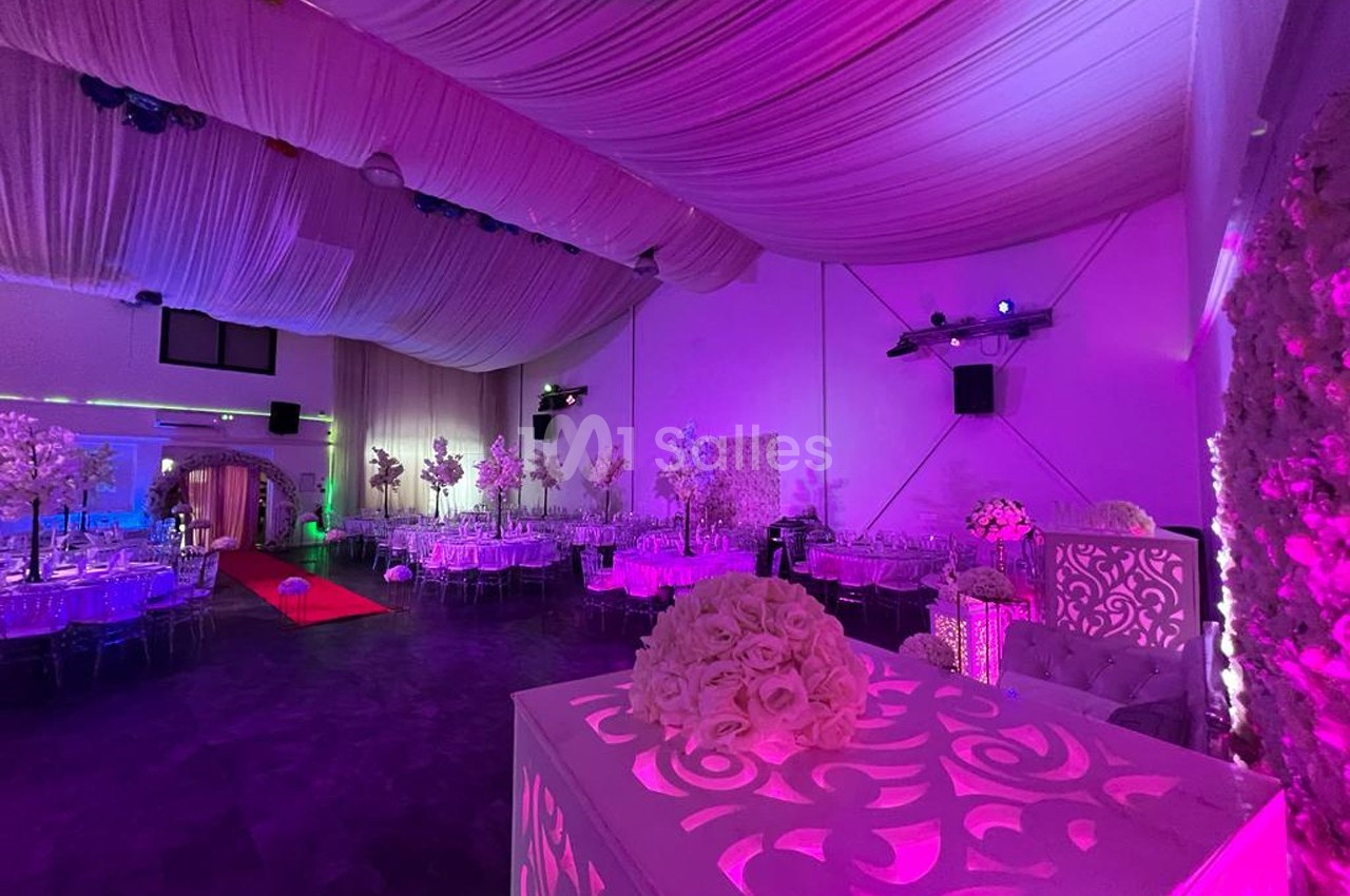 Salle de réception décorée avec des tables dressées, éclairage rose et plafond drapé.