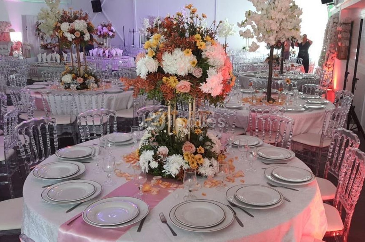 Table ronde décorée pour un événement, avec nappes blanches, vaisselle élégante et centre de table floral coloré.