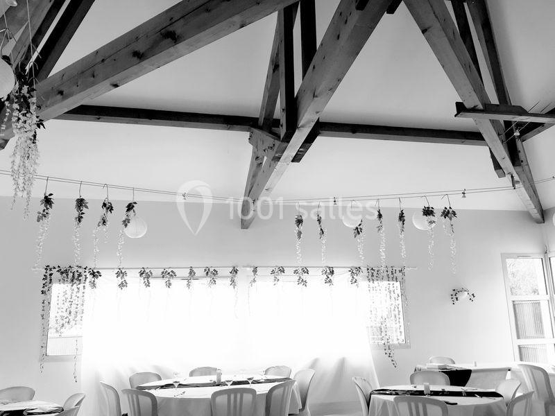 Plafond avec poutres apparentes en bois, décoré de guirlandes végétales, au-dessus de tables dressées dans une salle…