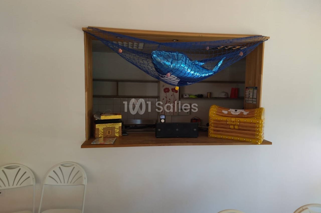 Un comptoir décoré avec un filet contenant un ballon en forme de baleine, des coffres et des chaises blanches devant.